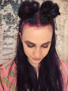 A woman with a glittery purple space bun half up half down hairstyle